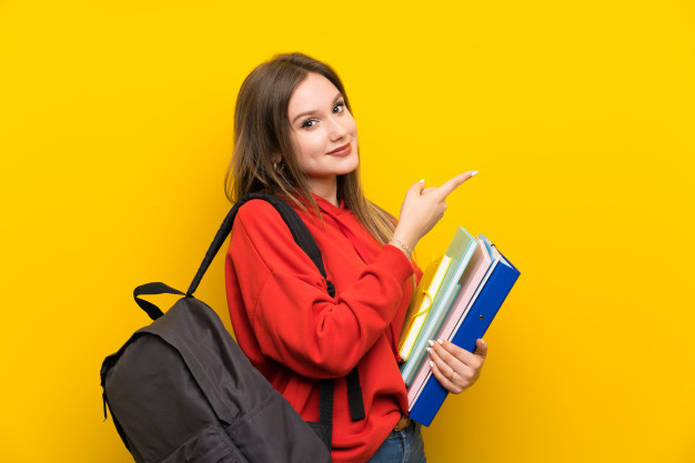 Jovem de, aproximadamente, 17 anos, em um fundo amarelo e vestindo um casaco alaranjado. Ela está com uma feição confiante e preparada para estudar e cumprir suas metas da semana. Ela está apontando para o local onde realizará o estudo e está com uma mochila marrom em suas costas e com pastas e cadernos em sua mão esquerda, apoiando-os no corpo.