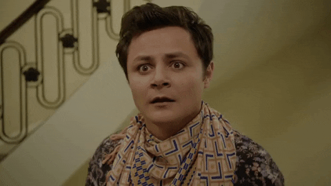 Gif (imagem com movimento), de um homem vestindo uma camisa estampada e um lenço no pescoço. Ele está fazendo gestos e feições de desespero e, logo em seguida, sai de cena.